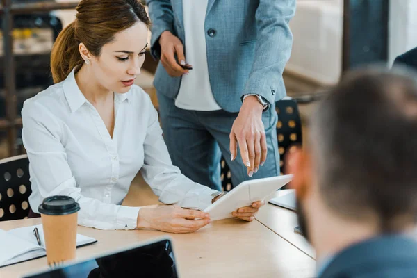 Cropped view of business coach pointing with finger at digital tablet near beautiful colleague — Stock Photo