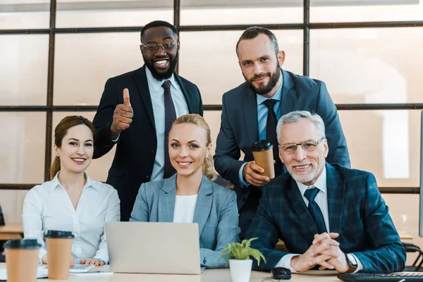 Allegro afro americano uomo mostrando pollice verso l'alto vicino ai colleghi in ufficio — Foto stock