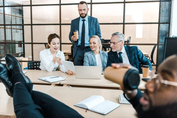 Enfoque selectivo de hombres de negocios alegres y mujeres de negocios mirando tableta digital cerca de compañero de trabajo afroamericano - foto de stock