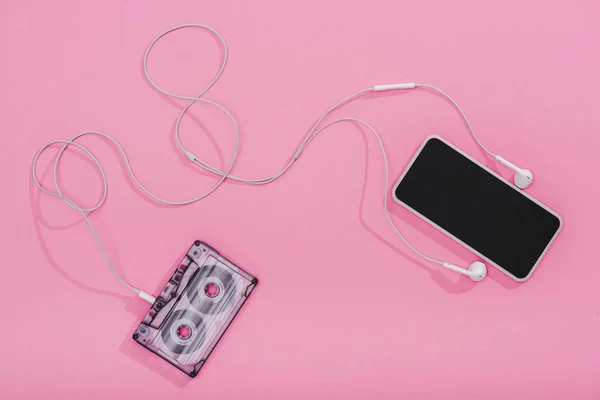 Vista superior de casete de audio vintage con auriculares y teléfono inteligente con pantalla en blanco en rosa - foto de stock