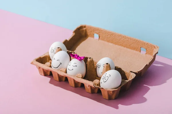 Eggs with various face expressions in egg carton on blue and pink — Stock Photo