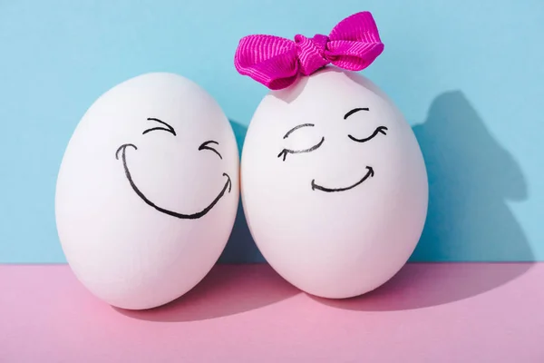 Egg with bow and egg with happy face expression on blue and pink — Stock Photo