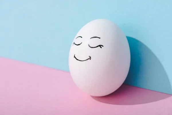 Egg with happy face expression on blue and pink with copy space — Stock Photo