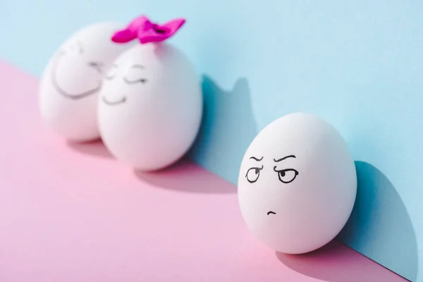 Селективный фокус яйца с сердитым выражением лица возле яиц со счастливыми лицами на голубом и розовом — стоковое фото