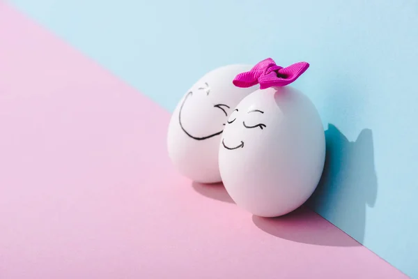 Egg with bow and egg with happy face expression on blue and pink with copy space — Stock Photo