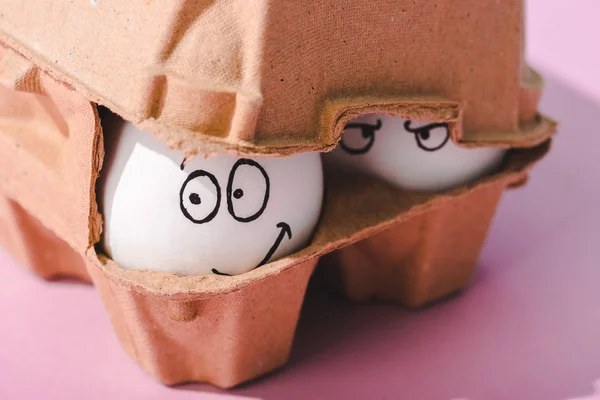 Primer plano de los huevos con expresiones faciales enojadas y sonrientes en cartón de huevo - foto de stock