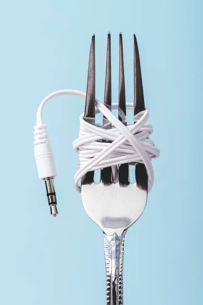 Close up view of earphones wrapped over metal fork isolated on blue, music concept — Stock Photo