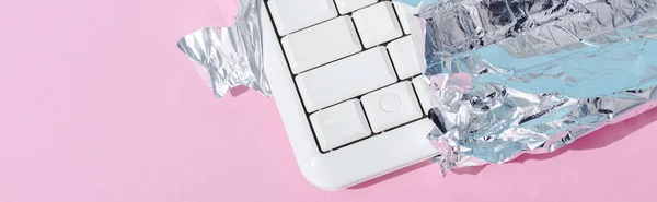 Cliché panoramique du clavier d'ordinateur enveloppé dans une feuille d'argent sur rose, concept Chocolate Bar — Photo de stock