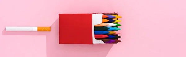 Plan panoramique de crayons colorés dans le paquet de cigarettes et cigarette de tabac sur rose, concept fumeur — Photo de stock