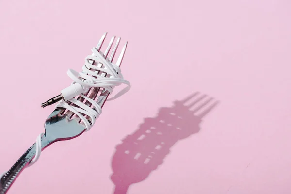 Earphones wrapped over metal fork on pink with copy space, music concept — Stock Photo