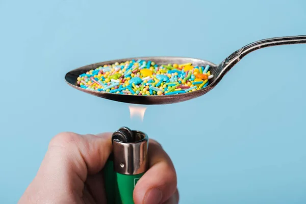 Vista recortada de hombre iluminación cuchara de metal con chispas de colores aislados en azul, concepto de adicción al azúcar - foto de stock