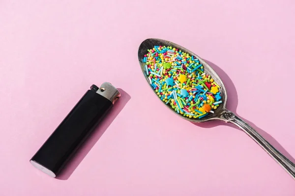 Vue de dessus de briquet et cuillère en métal avec des saupoudres colorées sur rose, concept de dépendance au sucre — Photo de stock