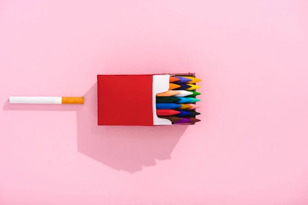 Вид зверху барвисті олівці в упаковці сигарет і тютюнова сигарета на рожевому, концепція куріння — стокове фото