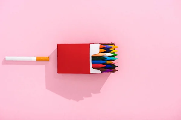 Top view of colorful crayons in cigarette pack and tobacco cigarette on pink, smoking concept — Stock Photo