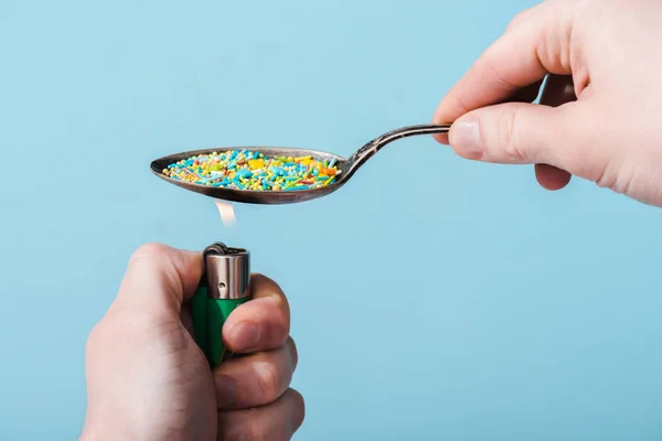 Vue recadrée de l'homme allumant une cuillère en métal avec des aspersions colorées isolées sur bleu, concept de dépendance au sucre — Photo de stock