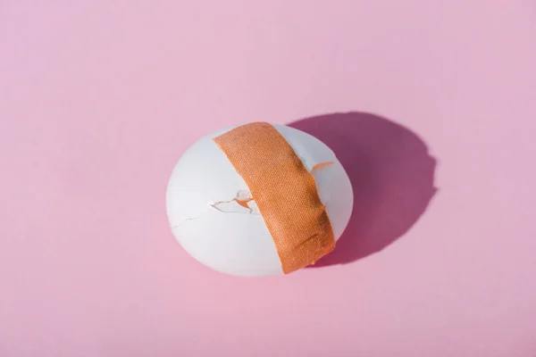 Top view of cracked egg with adhesive medical plaster on pink — Stock Photo