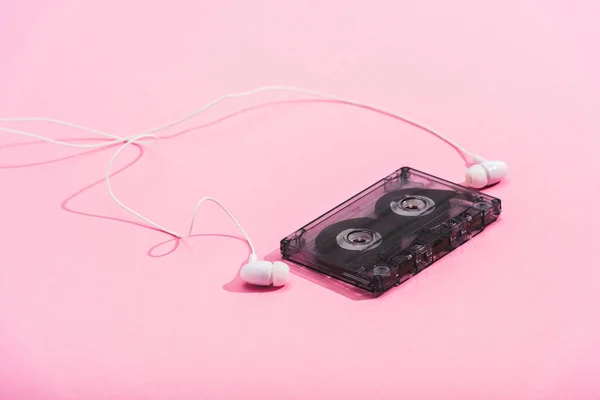 Plastic vintage audio cassette with earphones on pink, music concept — Stock Photo