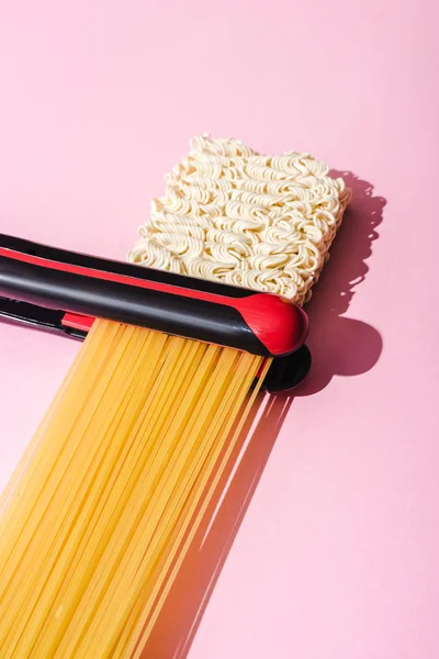 Fer plat, spaghettis et nouilles instantanées ondulées sur rose, concept de lissage des cheveux — Photo de stock