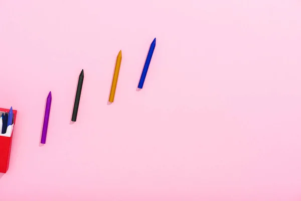 Top view of colorful crayons in row and cigarette pack on pink with copy space, smoking concept — Stock Photo