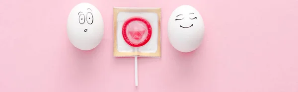 Panoramic shot of eggs with happy and surprised face expressions with condom wrapped as lollipop on pink — Stock Photo