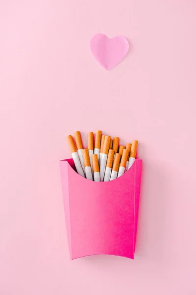 Vue du dessus des cigarettes emballées dans une boîte en papier rose avec symbole coeur, concept de frites — Photo de stock