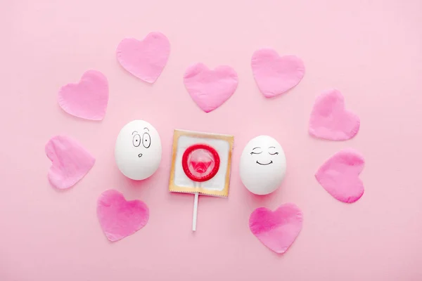 Top view of eggs with happy and surprised face expressions, paper hearts and condom wrapped as lollipop on pink — Stock Photo