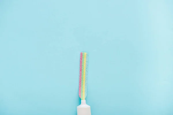 Vue du dessus du tube de dentifrice avec des bonbons colorés à mâcher isolés sur bleu avec espace de copie — Photo de stock