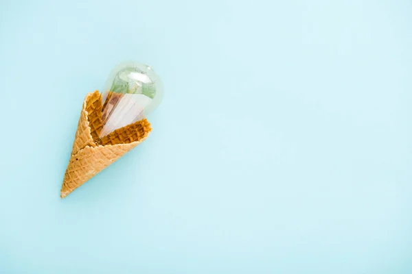 Top view of glass lightbulb in ice cream cone isolated on blue with copy space — Stock Photo