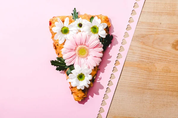 Vista superior de fatia de pizza com flores em papel rosa com corações cortados na mesa de madeira — Fotografia de Stock