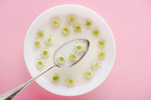 Vue du dessus de la cuillère et des fleurs de chrysanthème dans un bol avec du porridge sur rose — Photo de stock