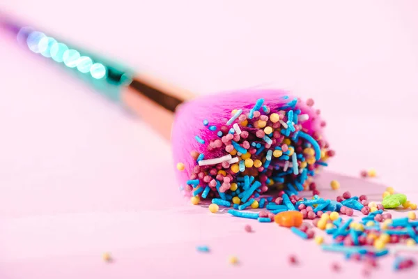 Close up view of makeup brush covered in colorful sprinkles on pink — Stock Photo