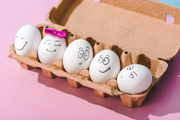 Ovos com diferentes expressões faciais na caixa de ovos em rosa — Fotografia de Stock