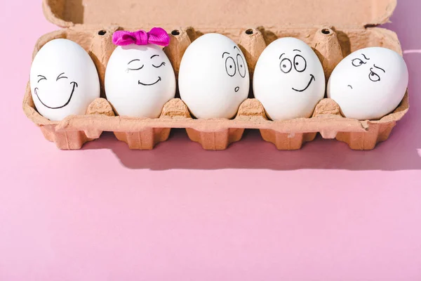 Huevos con diferentes expresiones faciales en cartón de huevo en rosa con espacio para copiar — Stock Photo