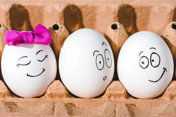 Primer plano de huevos con expresiones faciales sonrientes y conmocionadas en cartón de huevo - foto de stock