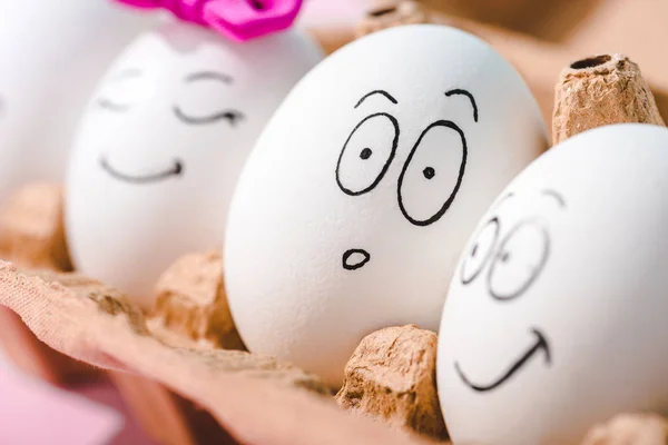 Vista de cerca de los huevos con diferentes expresiones faciales en cartón de huevo - foto de stock