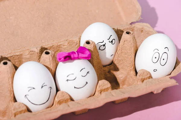 Huevos con varias expresiones faciales en cartón de huevo en rosa - foto de stock