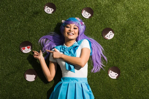 Asian anime girl in purple wig with emoticons lying on grass — Stock Photo