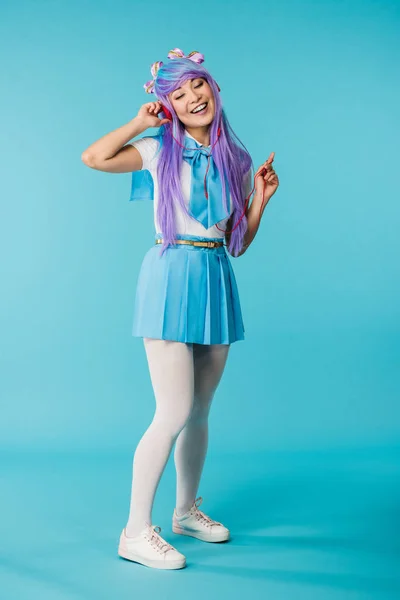 Вид в полный рост аниме девушки в парике, слушающей музыку в наушниках с закрытыми глазами на голубом фоне — стоковое фото