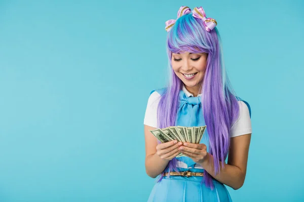 Asian anime girl in purple wig counting dollar banknotes isolated on blue — Stock Photo