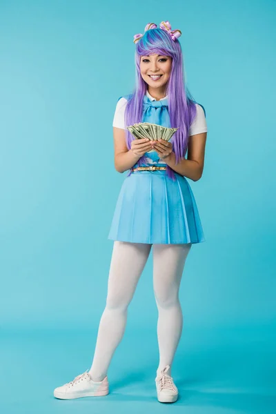 Opinião cheia do comprimento da menina asiática do anime na peruca roxa que conta notas de banco do dólar no azul — Fotografia de Stock