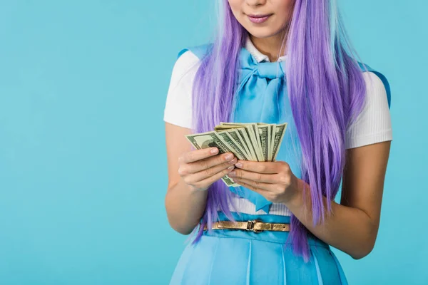 Обрізаний вид аніме-дівчини в фіолетовій перуці, що рахує доларові банкноти ізольовані на синьому — стокове фото