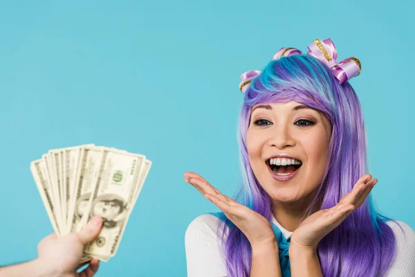 Обрезанный вид человека с долларовыми банкнотами и возбужденной азиатской аниме-девушкой, изолированной на голубом — стоковое фото