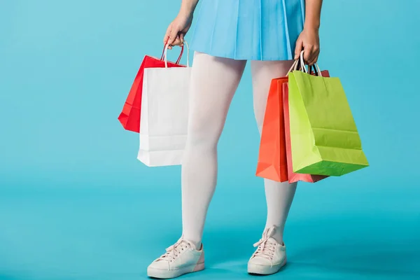 Cropped view of girl in skirt and white pantyhose holding shopping bags on blue — Stock Photo