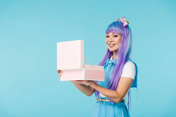 Smiling asian anime girl holding open briefcase isolated on blue — Stock Photo
