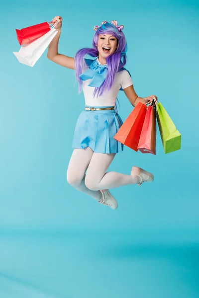 Захоплена азіатська аніме дівчина в перуці стрибає з сумками на синьому — стокове фото