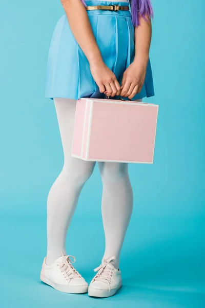 Cropped view of girl in skirt holding briefcase on blue — Stock Photo