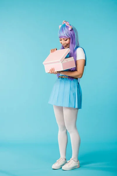 Vista completa de la chica anime en peluca púrpura celebración maletín en azul - foto de stock