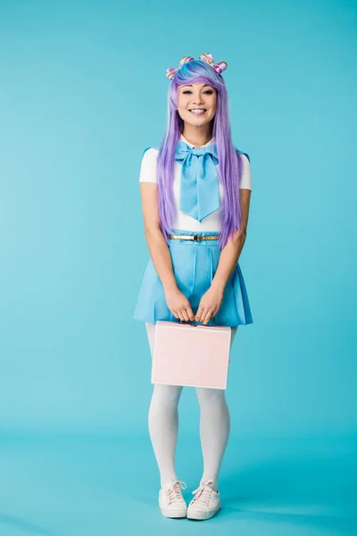 Visão de comprimento total da menina anime em roxo peruca segurando pasta em azul — Fotografia de Stock
