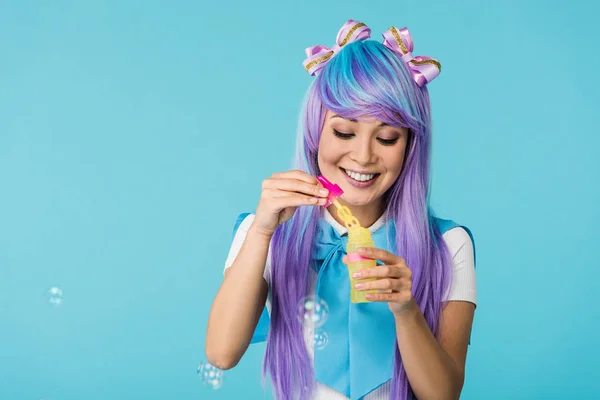Азиатская девушка аниме в фиолетовом парике с мыльными пузырями, изолированными на голубом — стоковое фото