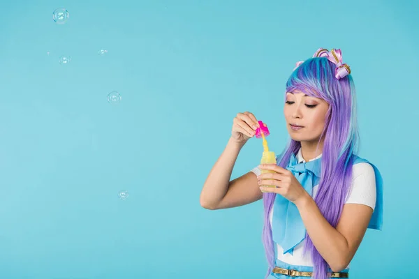 Chica anime asiático en peluca púrpura con burbujas de jabón aislado en azul - foto de stock
